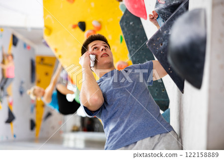 Young man talking on phone while exercising in climbing gym 122158889