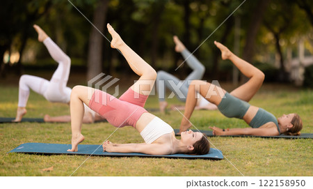 Yoga lesson visitors girls perform Setu Badha Sarvangasana in park 122158950