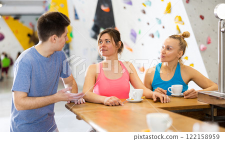 Two sports women and a guy communicate after training on a climbing wall at a table in cafe Two sports women and a guy communicate after training on a climbing wall at a table in cafe 122158959