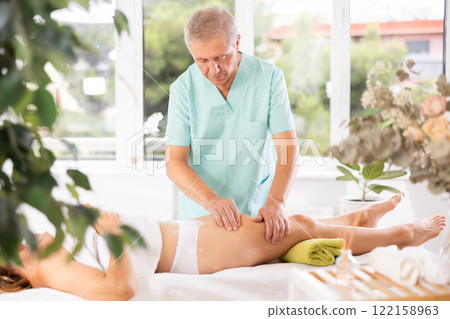 Skilled old masseur conducting hip massage for woman client 122158963