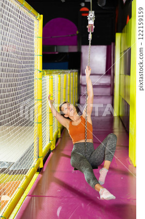 Excited woman swinging on indoor zip line at modern play center Excited woman swinging on indoor zip line at modern play center 122159159