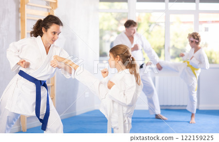 Preteen girl in kimono practicing karate kicks during sparring with mother 122159225