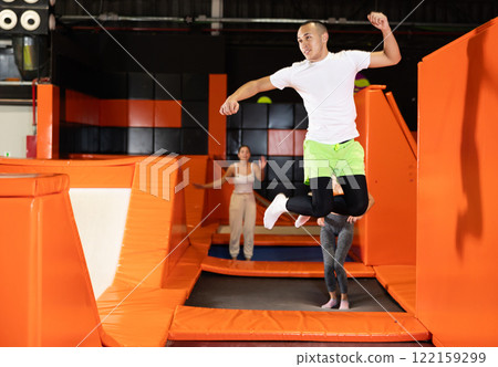 Joyful young man jumping on trampolines in colorful amusement park 122159299