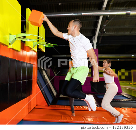 Athletic people throw ball into basketball basket while jumping on trampolines at an entertainment center 122159330