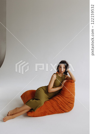 Woman in green tight dress sitting on red bean bag chair on white background 122159532