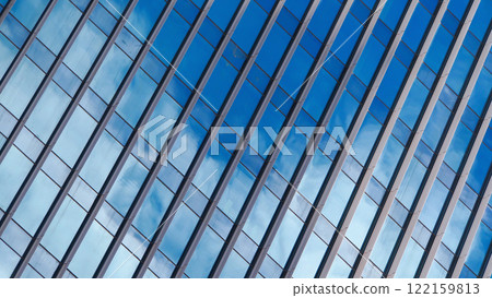 An abstract view of a modern building facade, featuring a grid of blue-tinted glass panels reflecting the sky. The diagonal lines add a dynamic element to the composition. 122159813