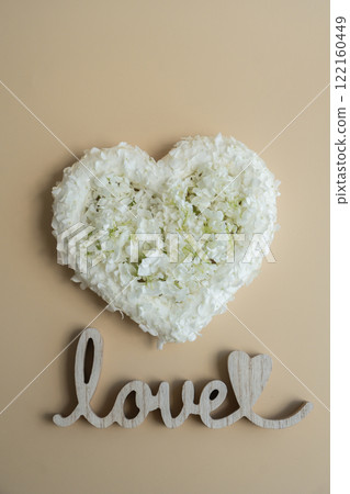 Heart made of white lilac flowers on pastel beige background Wooden word LOVE. Still life romantic composition of Valentines day holiday copy space for your text invitation greeting card 122160449