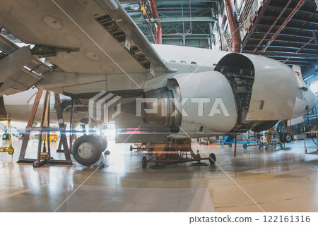 Close-up of a white passenger jet plane with its engine open in the aircraft hangar. Airliner under maintenance. Checking mechanical systems for flight operations 122161316