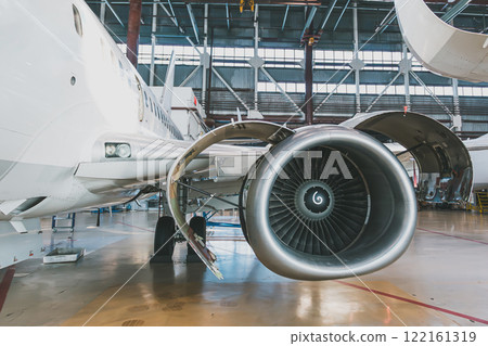 White passenger jet plane in the aviation hangar. Aircraft under maintenance. Checking mechanical systems for flight operations 122161319