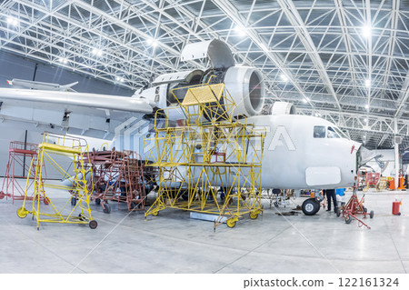 White transport aircraft in the hangar. Airplane under maintenance. Checking mechanical systems for flight operations 122161324