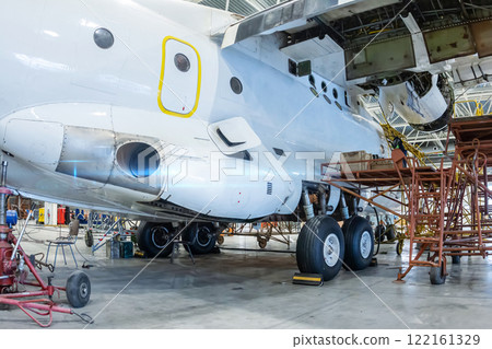 White transport airplane in the hangar. Aircraft under maintenance. Checking mechanical systems for flight operations 122161329