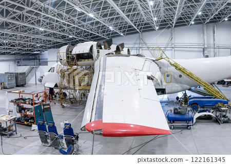 White transport airplane in the aviation hangar. Aircraft under maintenance. Checking mechanical systems for flight operations White transport airplane in the aviation hangar. Aircraft under maintenance. Checking mechanical systems for flight operations 122161345