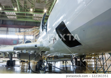 White passenger aircraft in the hangar. Airplane under maintenance. Checking mechanical systems for flight operations White passenger aircraft in the hangar. Airplane under maintenance. Checking mechanical systems for flight operations 122161351