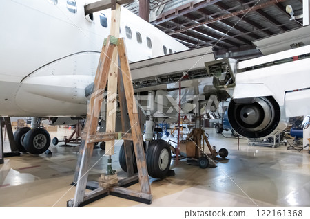 White passenger jetliner in the aviation hangar. Jet plane under maintenance. Checking mechanical systems for flight operations 122161368