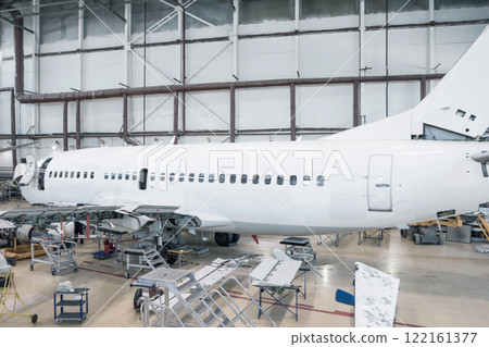 White passenger airliner in the hangar. Jetliner under maintenance. Checking mechanical systems for flight operations White passenger airliner in the hangar. Jetliner under maintenance. Checking mechanical systems for flight operations 122161377