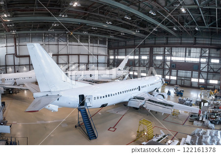 White passenger airplanes in the aviation hangar. Aircrafts under maintenance. Checking mechanical systems for flight operations 122161378