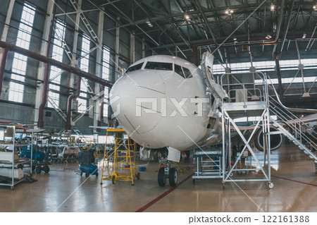 White passenger airliner in the aircraft hangar. Airplane under maintenance. Checking mechanical systems for flight operations 122161388