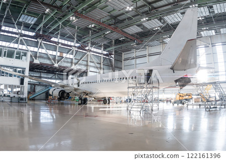 White passenger airliner in the aviation hangar. Airplane under maintenance. Checking mechanical systems for flight operations 122161396
