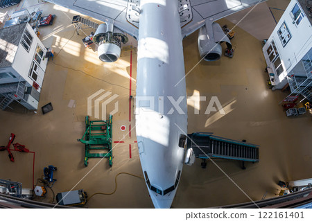 Top view of a white passenger airliner in the aviation hangar. Aircraft under maintenance. Checking mechanical systems for flight operations Top view of a white passenger airliner in the aviation hangar. Aircraft under maintenance. Checking mechanical systems for flight operations 122161401