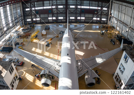 Top view of a white passenger jet plane in the aviation hangar. Airliner under maintenance. Checking mechanical systems for flight operations Top view of a white passenger jet plane in the aviation hangar. Airliner under maintenance. Checking mechanical systems for flight operations 122161402