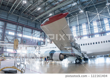 White passenger aircraft in the aviation hangar. Airplane under maintenance. Checking mechanical systems for flight operations 122161404
