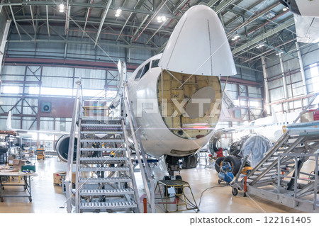 Front view of the white passenger airplane under maintenance in the aviation hangar. The aircraft has opened weather radar. Checking mechanical systems for flight operations 122161405