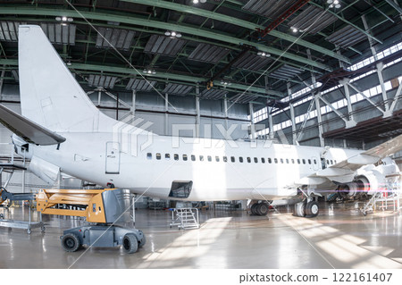 White passenger jetliner in the aviation hangar. Jet plane under maintenance. Checking mechanical systems for flight operations 122161407