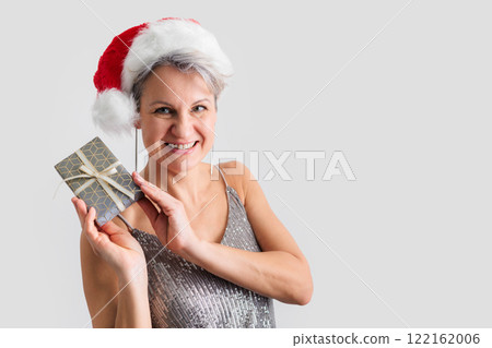 Elderly beautiful smiling middle-aged woman in Santa Claus hat holding gift in hands 122162006