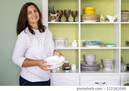 Smiling woman utensil crockery storage organizing method at white vintage shelf closet Smiling woman utensil crockery storage organizing method at white vintage shelf closet 122162080