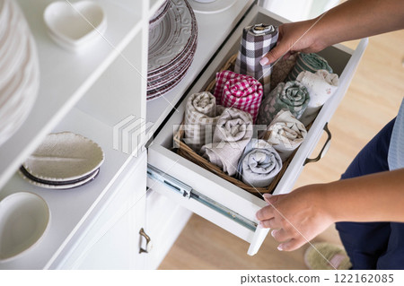 Woman placing kitchen textile towel roll in whicked basket shelf rustic retro commode top view Woman placing kitchen textile towel roll in whicked basket shelf rustic retro commode top view 122162085