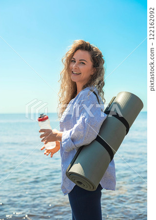 Smiling young fitness yoga woman drink pure water blue sea sky beach coastline closeup Smiling young fitness yoga woman drink pure water blue sea sky beach coastline closeup 122162092