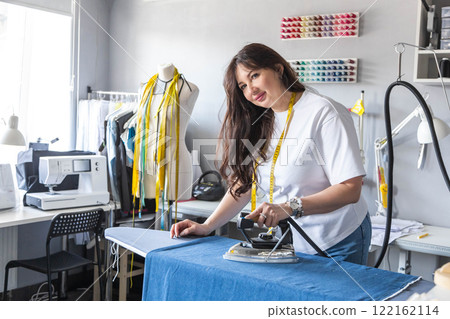 A woman dressmaker steams and irons fabric for cutting and sewing clothes. 122162114