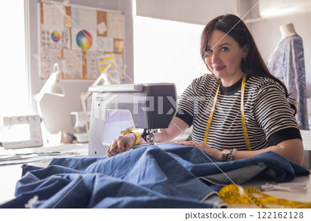 Woman plus size fashion designer uses a sewing machine in her studio.  122162128
