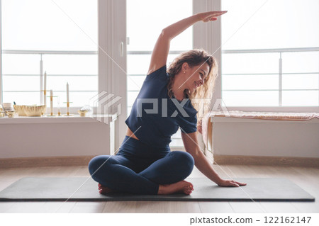 Yoga woman stretching body with raising hand sitting on mat at home panorama window 122162147