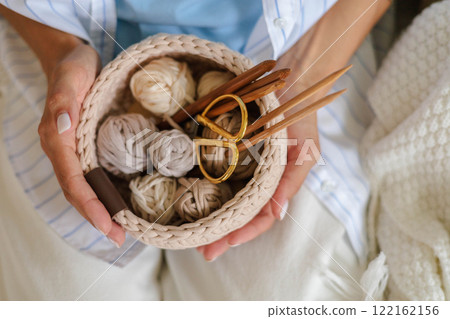 A woman in stylish clothes holds a crocheted basket with skeins of cotton yarn in natural tones A woman in stylish clothes holds a crocheted basket with skeins of cotton yarn in natural tones 122162156