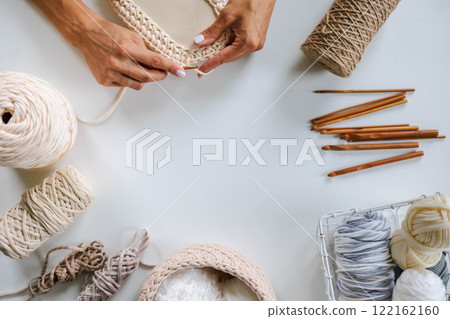 Women's hands knitting a basket from beige yarn. Crochet hooks. Skeins of yarn of natural shades. 122162160
