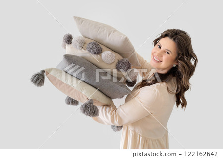 Beautiful European woman in beige suit holds Stack of decorative stylish pillows. White background. 122162642