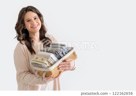 Beautiful European woman in beige suit holds wicker stylish basket with neatly folded pillowcases Beautiful European woman in beige suit holds wicker stylish basket with neatly folded pillowcases 122162656