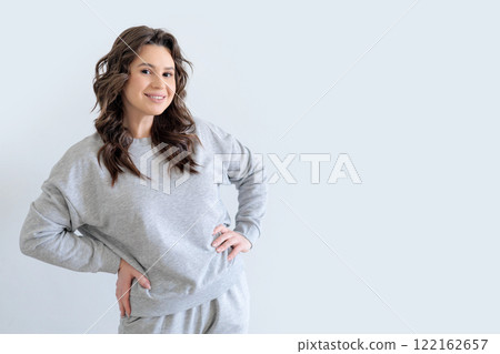 Beautiful European woman in gray knitted suit smiles and keeps hands on hips. White background. Beautiful European woman in gray knitted suit smiles and keeps hands on hips. White background. 122162657