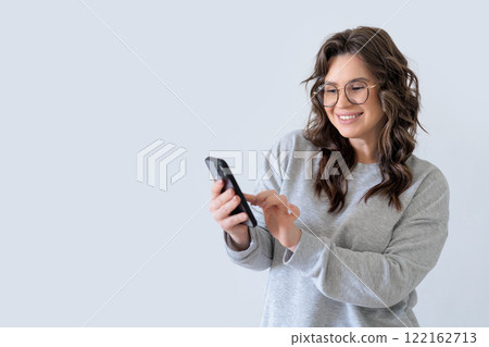 Beautiful European woman in gray knitted suit smiles and writes a message in messenger on smartphone 122162713