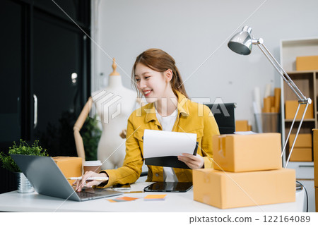 Young business owner woman prepare parcel box and standing check online orders for deliver to customer on tablet, laptop 122164089