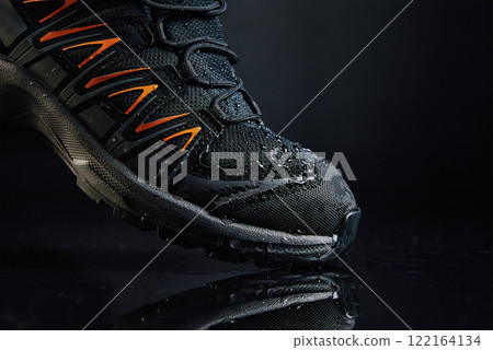 Close-up of waterproof black hiking boot with orange accents and water droplets. Rugged trekking shoe on dark background. Footwear for exploration and outdoor activities Close-up of waterproof black hiking boot with orange accents and water droplets. Rugged trekking shoe on dark background. Footwear for exploration and outdoor activities 122164134