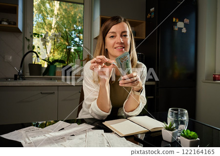 Woman holding stack of hundred dollar bills on table filled with receipts and financial bills. Concept of personal finances and planning home budget Woman holding stack of hundred dollar bills on table filled with receipts and financial bills. Concept of personal finances and planning home budget 122164165