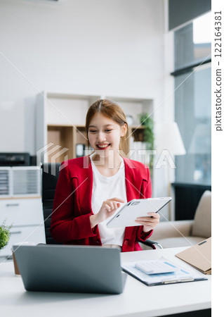 Confident Asian woman with a smile standing holding notepad and tablet at the ffice. 122164381