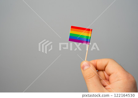 Hand holding a small LGBT rainbow flag. Diversity and inclusiveness of society, sexual minorities and LGBT. Protection of human rights and freedoms. Development of society 122164530