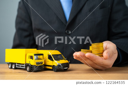 Businessman holds stacks of coins in outstretched hand and truck with delivery van. Profit from the transport company, industry. Profitability of courier deliveries and transportation. 122164535