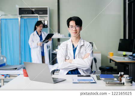 Confident young male doctor in white medical uniform sit at desk working on computer 122165025