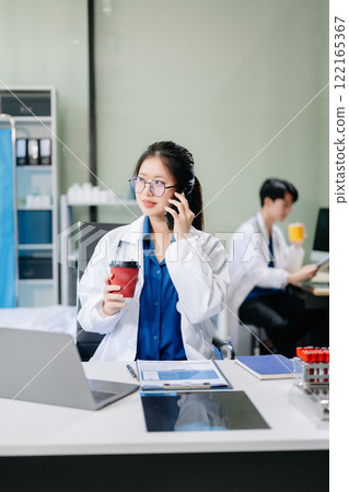 Confident young female doctor in white medical uniform sit at desk working on computer. Confident young female doctor in white medical uniform sit at desk working on computer. 122165367