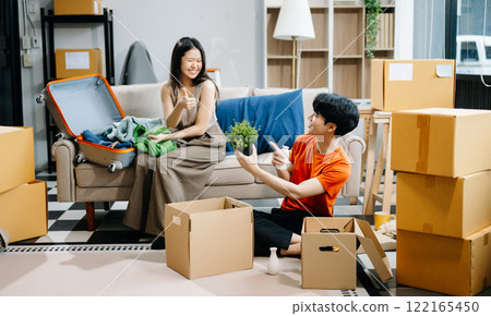 Asian young attractive couple man and woman use tablet and smartphone online shopping furniture decorate house with carton package move 122165450