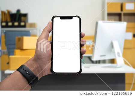 Hand holding white mobile phone with blank white screen in office. 122165639
